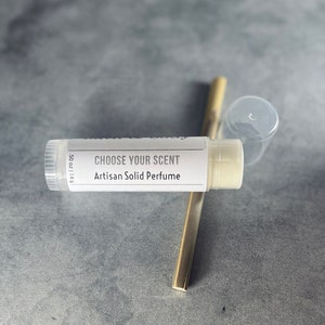 May include: A white tube of solid perfume with the text "CHOOSE YOUR SCENT Artisan Solid Perfume" and "0.5 oz | 14g".