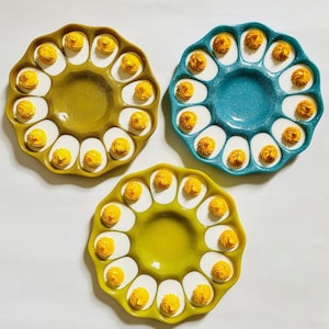 Può includere: Tre portapiatti per uova, uno blu-verde, due giallo senape, con incavi a forma di uovo bianchi e cucchiaiate di ripieno di uova ripiene giallo.