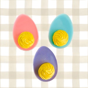 Könnte beinhalten: Drei gefüllte Eier, jedes mit einer anderen Schalenfarbe: rosa, blau und lila. Die Eier sind mit einem Strudel aus gelbem Eigelb gefüllt.