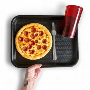 Op de afbeelding: Een pepperoni pizza op een zwart dienblad met een rode beker en een vork. De pizza heeft een gouden korst en is belegd met ronde plakjes pepperoni. De rode beker is gevuld met een donkere vloeistof.