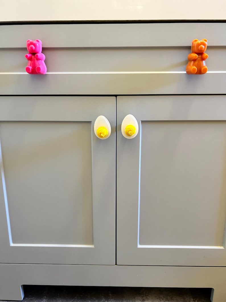 May include: A set of cabinet hardware featuring a pink bear, an orange bear, and two white egg-shaped knobs with yellow accents.
