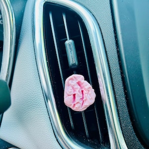 Puede incluir: Un ambientador de coche de chicle rosa colgado de la ventilación de un coche.