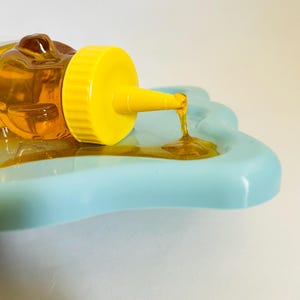 May include: A yellow squeeze bottle with a clear, honey-colored liquid pouring onto a light blue, star-shaped dish.