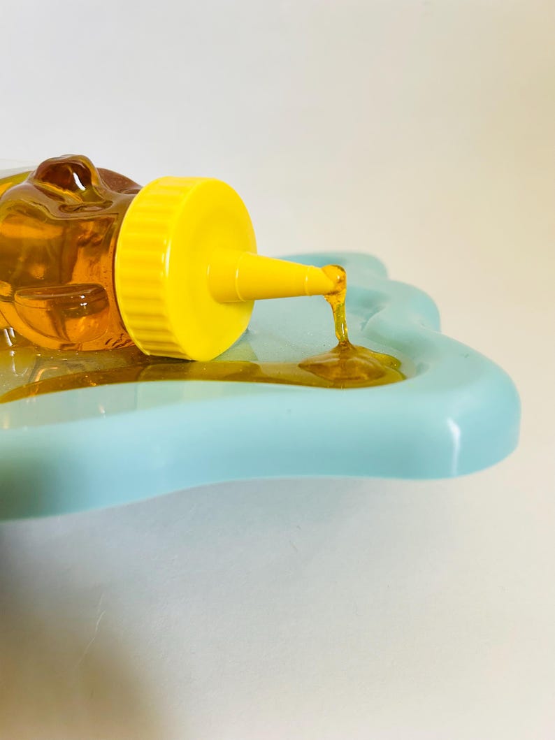 May include: A yellow squeeze bottle with a clear, honey-colored liquid pouring onto a light blue, star-shaped dish.
