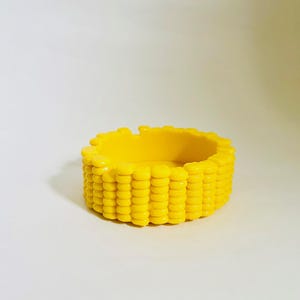 May include: A yellow corn cob shaped ceramic dish. The dish is made to look like a corn cob with rows of kernels.