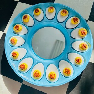 May include: A blue egg tray with a mirror in the center. The tray is filled with deviled eggs, each with a yellow yolk and a brown swirl on top.