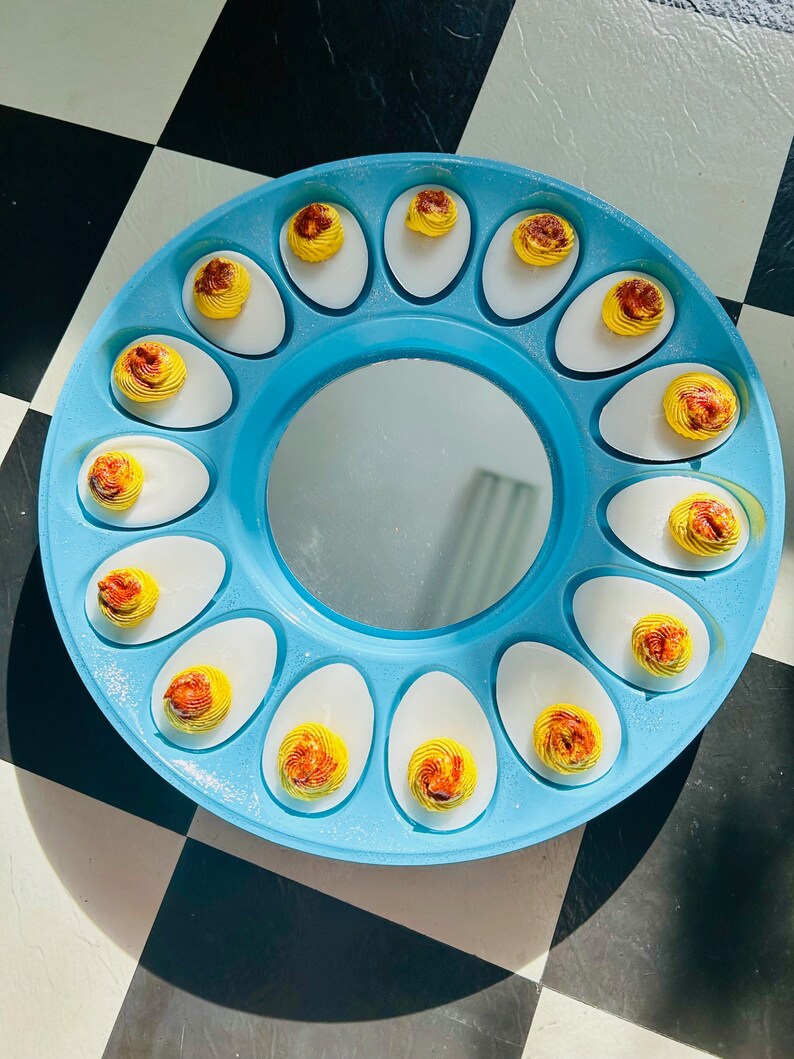 May include: A blue egg tray with a mirror in the center. The tray is filled with deviled eggs, each with a yellow yolk and a brown swirl on top.