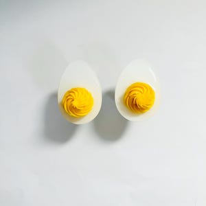 May include: Two white ceramic egg cups with yellow egg yolk filling. The yolk is swirled and piped into a decorative shape.