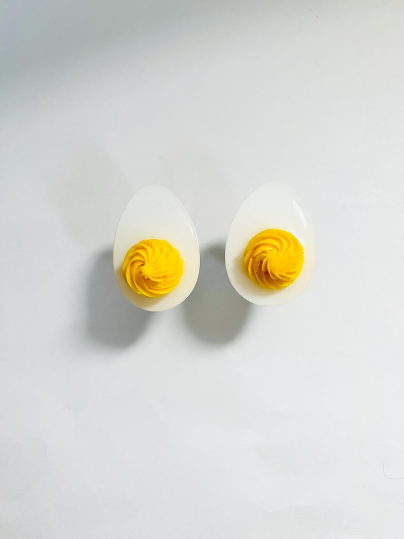 May include: Two white ceramic egg cups with yellow egg yolk filling. The yolk is swirled and piped into a decorative shape.