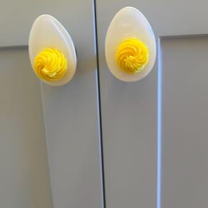 May include: Two white ceramic cabinet knobs shaped like eggs with yellow swirls on the top.