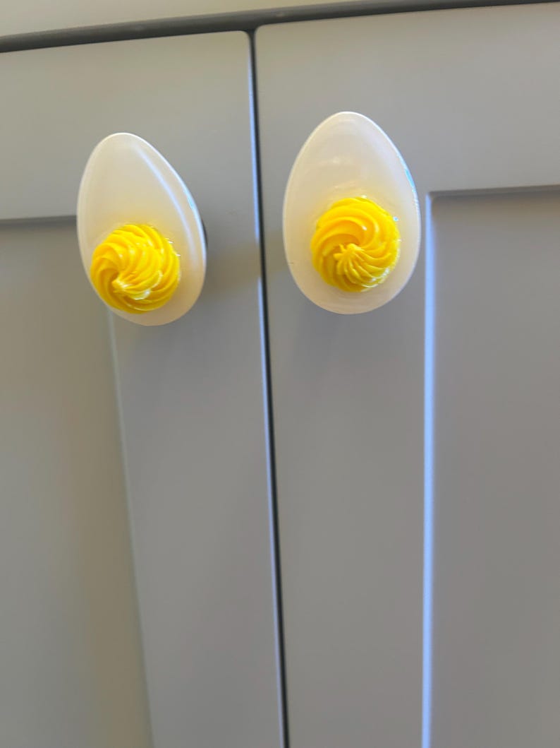 May include: Two white ceramic cabinet knobs shaped like eggs with yellow swirls on the top.