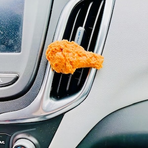May include: A fried chicken wing air freshener hanging from the air vent of a car's dashboard.
