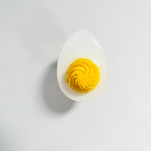 May include: A deviled egg with a swirl of yellow yolk in a white ceramic egg cup.