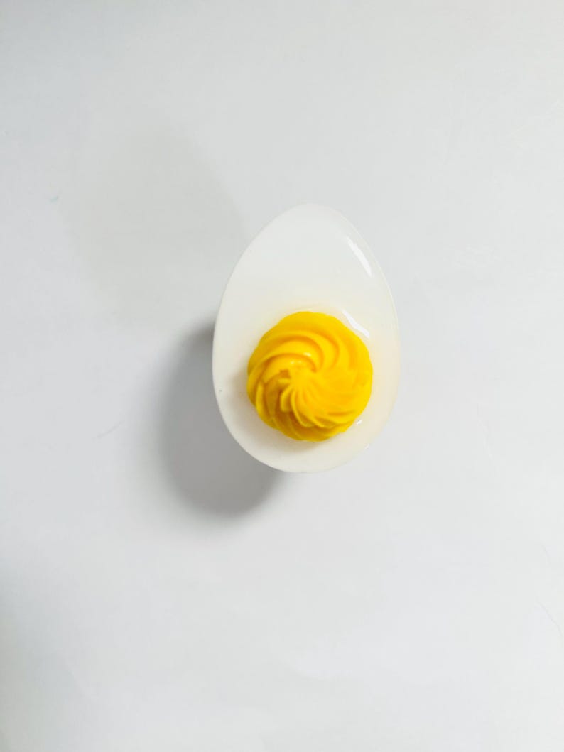 May include: A deviled egg with a swirl of yellow yolk in a white ceramic egg cup.