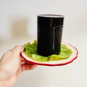 May include: A black glass jar with a lid, sitting on a white plate with a green lettuce leaf.