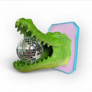 Pode incluir: Escultura de um jacar&eacute; verde segurando uma bola de discoteca prateada. O jacar&eacute; &eacute; montado em uma placa retangular rosa e azul. A escultura tem uma apar&ecirc;ncia texturizada e escamosa.