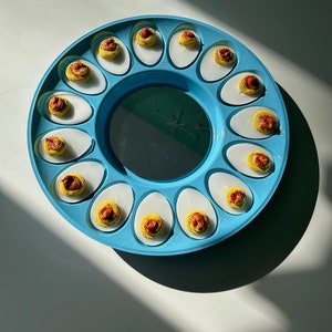 May include: A blue plastic egg tray with 12 deviled eggs. The eggs are filled with a yellow yolk and a red and orange paprika topping.