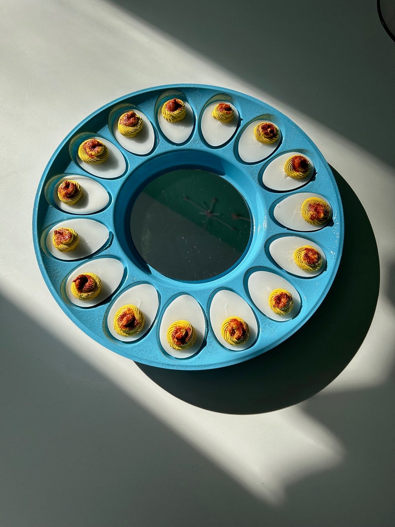 May include: A blue plastic egg tray with 12 deviled eggs. The eggs are filled with a yellow yolk and a red and orange paprika topping.