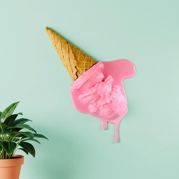 May include: A decorative wall art piece featuring a tan waffle cone with a large scoop of bright pink melting ice cream dripping downward. The textured cone has a classic grid pattern, while the pink ice cream has a smooth, glossy finish.
