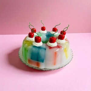 May include: A multi-coloured jelly dessert, decorated with whipped cream and vibrant red cherries. The jelly is presented on a clear, scalloped-edge glass plate against a pink backdrop. A cheerful and celebratory treat.