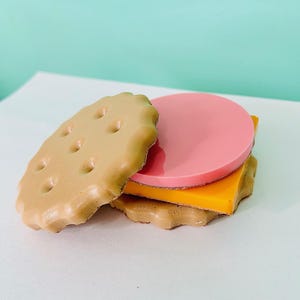May include: A pretend sandwich made of two brown sugar cookies, a slice of pink and a slice of yellow.