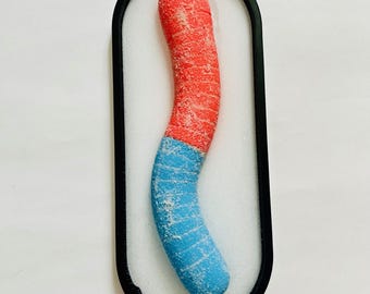 May include: A red and blue candy cane shaped object encased in a black oval frame. The candy cane is displayed on a white background.
