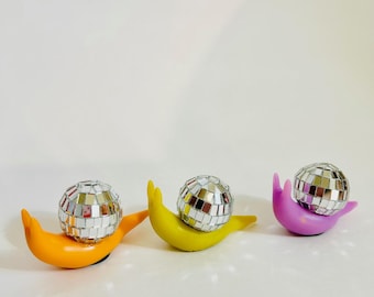 May include: Three decorative snails with mirrored disco ball shells. The snails are orange, yellow, and purple.