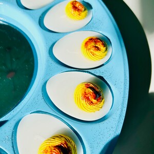 May include: A blue egg tray with six deviled eggs. The eggs are topped with a yellow and brown swirl.