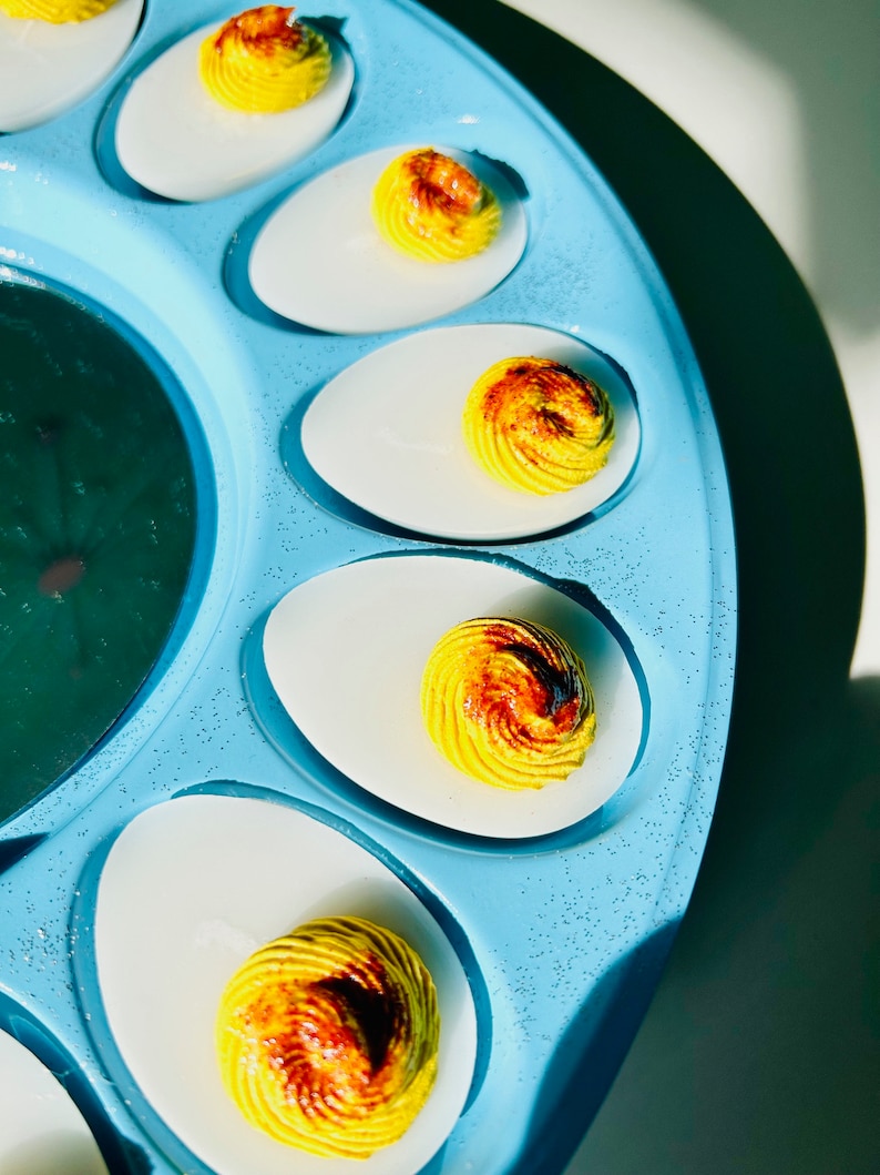 May include: A blue egg tray with six deviled eggs. The eggs are topped with a yellow and brown swirl.