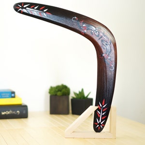 May include: A wooden boomerang with a black and brown finish and red and white painted designs. The boomerang is on a wooden stand.