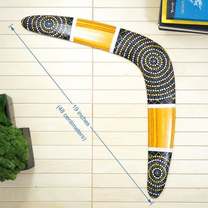 K&ouml;nnte beinhalten: Ein schwarzes und gelbes Bumerang mit wei&szlig;en Punkten und konzentrischen Kreisen. Das Bumerang ist 19 Zoll (48 Zentimeter) lang.