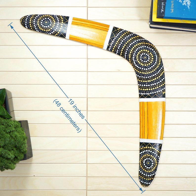 K&ouml;nnte beinhalten: Ein schwarzes und gelbes Bumerang mit wei&szlig;en Punkten und konzentrischen Kreisen. Das Bumerang ist 19 Zoll (48 Zentimeter) lang.