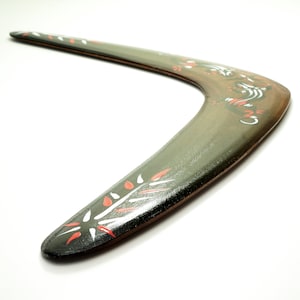 May include: A green wooden boomerang with red and white painted designs. The boomerang is curved and has a smooth surface.