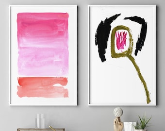 May include: Two framed abstract watercolour paintings. One features a gradient of pink and red hues, the other a black and green abstract shape on a white background. The paintings are displayed above a shelf with decorative items.