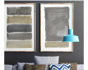 May include: A modern living room scene featuring a gray sofa with brown and patterned pillows. Two framed watercolor art pieces hang on the dark gray wall. A turquoise pendant light hangs above a white coffee table with decorative items.