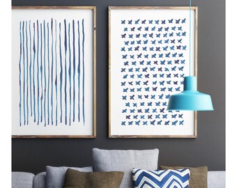 May include: A modern living room scene featuring a gray sofa with brown and patterned pillows. Two framed art prints with blue abstract designs hang on the dark gray wall. A light blue pendant lamp hangs above a white coffee table with a black metal bowl.