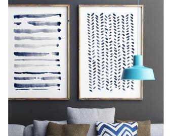 May include: A modern living room scene featuring two framed abstract art prints with blue watercolor designs. A light blue pendant lamp hangs above a gray sofa with brown and blue accent pillows. A white coffee table holds decorative items.