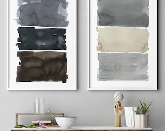 May include: Two framed abstract watercolor art prints. One features three horizontal bands of dark blue, black, and brown. The other has gray, beige, and light blue bands. The prints are displayed above a shelf with decorative items.