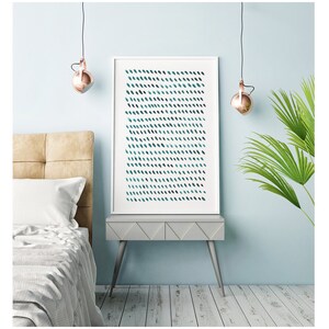 May include: A framed abstract art print featuring a pattern of teal and dark blue brushstrokes on a white background. The artwork is displayed on a gray nightstand in a bedroom setting. The room has light blue walls and a bed with a beige headboard.