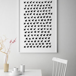 May include: A framed art print featuring a pattern of black butterfly-like shapes on a white background. The artwork is displayed above a white table with minimalist decor, including a vase and white ceramic pieces. A white chair is also visible.