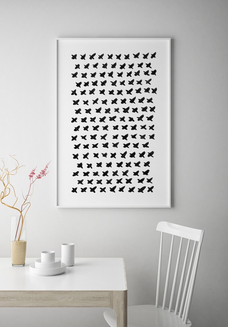 May include: A framed art print featuring a pattern of black butterfly-like shapes on a white background. The artwork is displayed above a white table with minimalist decor, including a vase and white ceramic pieces. A white chair is also visible.