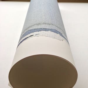 May include: Rolled artwork featuring a watercolor design. The cylindrical piece displays a light blue and gray textured pattern with blue and black horizontal bands. The bottom edge is a cream color, and the end is a tan color.