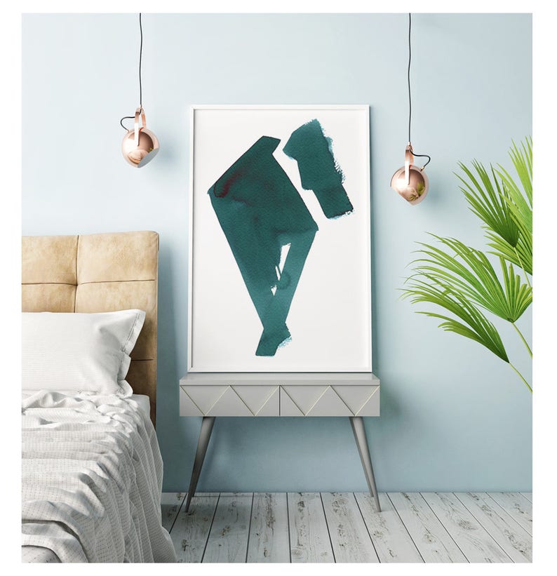 May include: Abstract teal watercolor art print in a white frame. The artwork features geometric shapes and brushstrokes. The print is displayed on a gray nightstand with a bed and a palm plant in the background. Copper pendant lights hang from the ceiling.