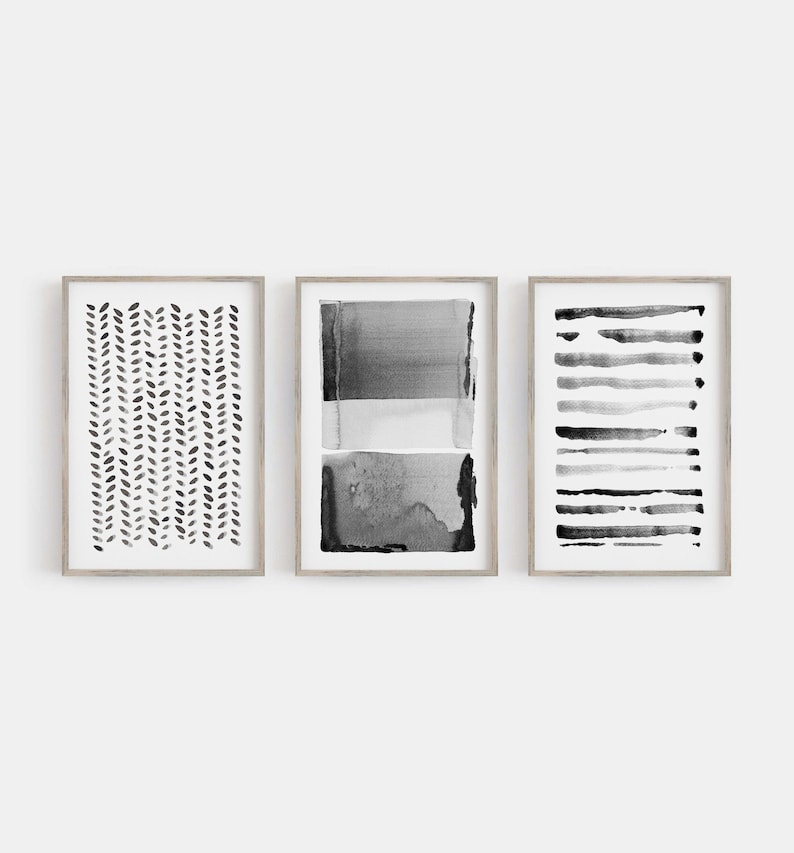 May include: Three framed abstract art prints. The prints feature black and gray watercolor designs. One print has a pattern of small, vertical leaf shapes. Another has horizontal bands of color. The third has a series of horizontal lines.