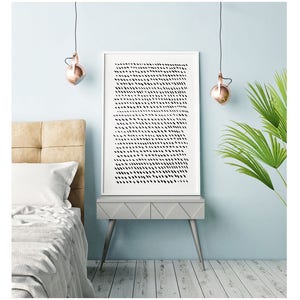 May include: A framed art print with a white border features a pattern of black dashes on a white background. The artwork rests on a gray nightstand with angled legs, next to a bed with a beige headboard. Copper-colored pendant lights hang above.