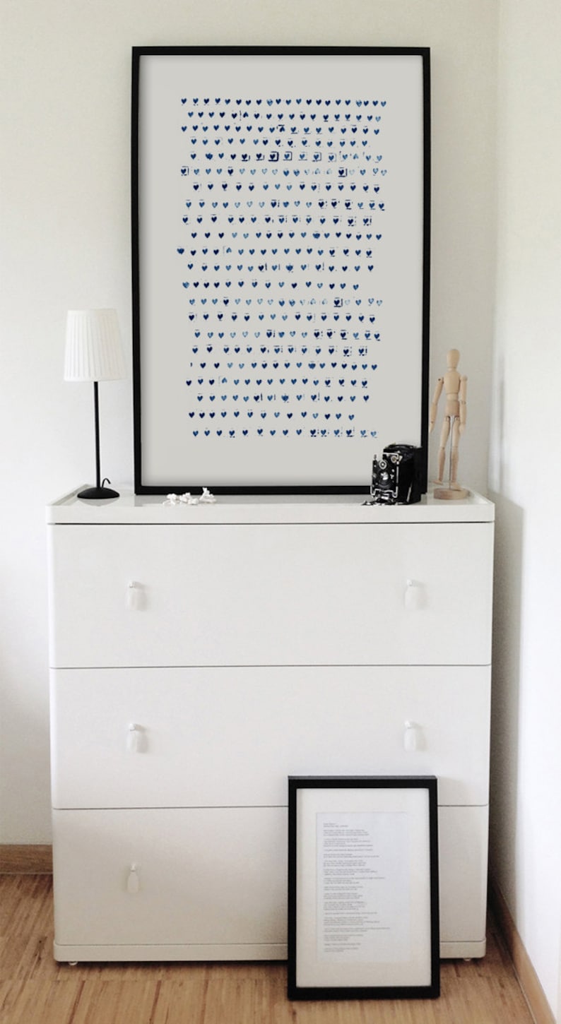 May include: A white dresser with three drawers, topped with a framed print of blue heart shapes. A small lamp, a vintage camera, and a wooden artist's mannequin are on the dresser. A framed print with text rests on the floor.