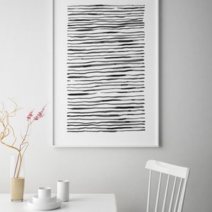 May include: A framed abstract art print featuring horizontal black lines of varying thickness and density on a white background. The artwork is displayed on a white wall above a white table with minimalist decor.