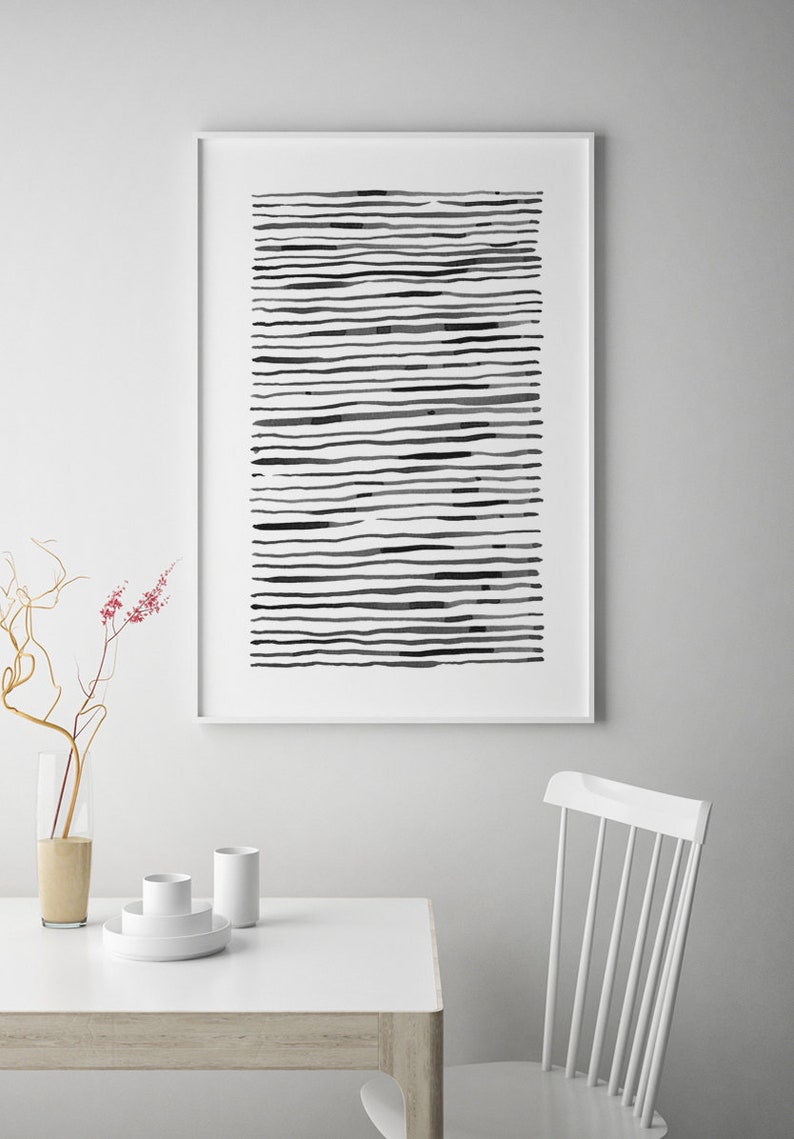 May include: A framed abstract art print featuring horizontal black lines of varying thickness and density on a white background. The artwork is displayed on a white wall above a white table with minimalist decor.