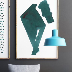 May include: Two framed abstract art prints with wooden frames. One print features a pattern of teal dots, and the other showcases a teal geometric shape. A turquoise pendant lamp hangs in the foreground, adding a pop of color.