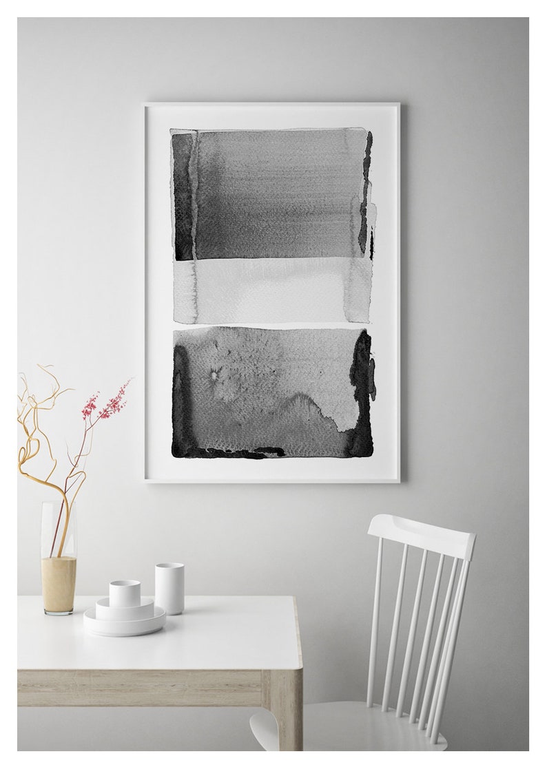 May include: Abstract black and white watercolor painting in a white frame. The artwork features three horizontal bands of varying shades of gray, creating a minimalist and modern aesthetic. The painting is displayed above a white table with a vase and tableware.